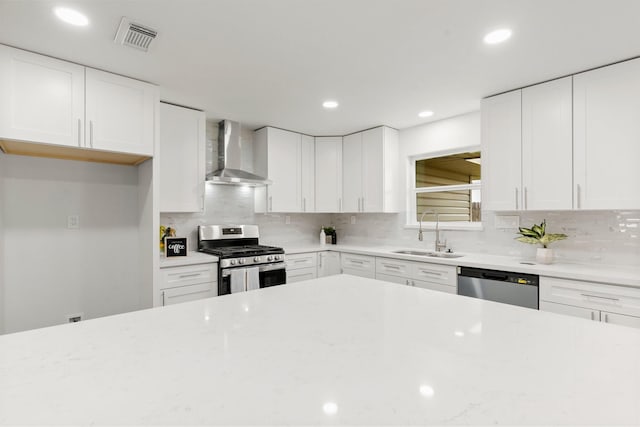 kitchen with wall chimney range hood, sink, appliances with stainless steel finishes, white cabinetry, and decorative backsplash