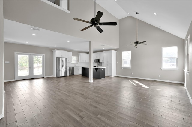 unfurnished living room featuring hardwood / wood-style flooring, high vaulted ceiling, ceiling fan, and french doors