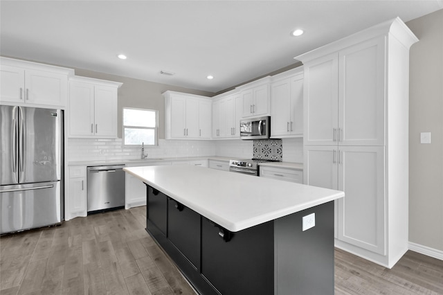 kitchen with sink, a center island, light wood-type flooring, appliances with stainless steel finishes, and white cabinets