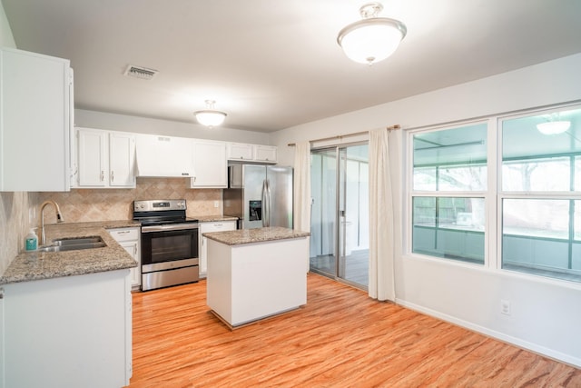 kitchen with appliances with stainless steel finishes, white cabinetry, sink, a center island, and light hardwood / wood-style flooring