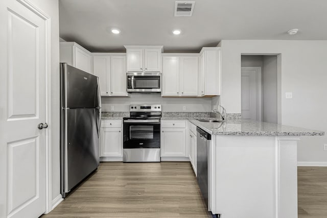 kitchen featuring visible vents, white cabinets, appliances with stainless steel finishes, a peninsula, and light stone countertops