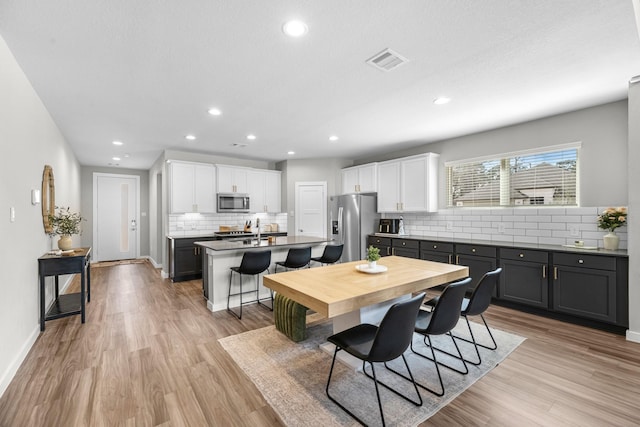 kitchen featuring an island with sink, stainless steel appliances, light wood-style floors, a breakfast bar area, and white cabinets