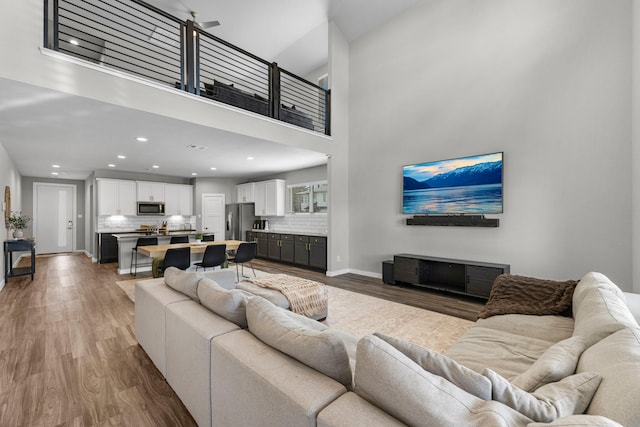 living area with recessed lighting, a high ceiling, baseboards, and wood finished floors