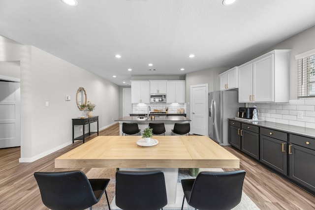 kitchen featuring a kitchen bar, gray cabinetry, stainless steel appliances, a kitchen island with sink, and white cabinets