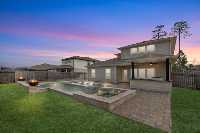 back house at dusk featuring ceiling fan, a swimming pool with hot tub, a patio area, and a lawn