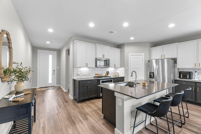 kitchen with gray cabinetry, sink, stainless steel appliances, and a center island with sink