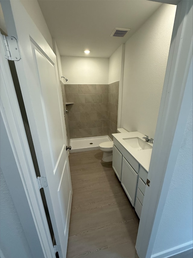 bathroom with vanity, hardwood / wood-style floors, toilet, and tiled shower