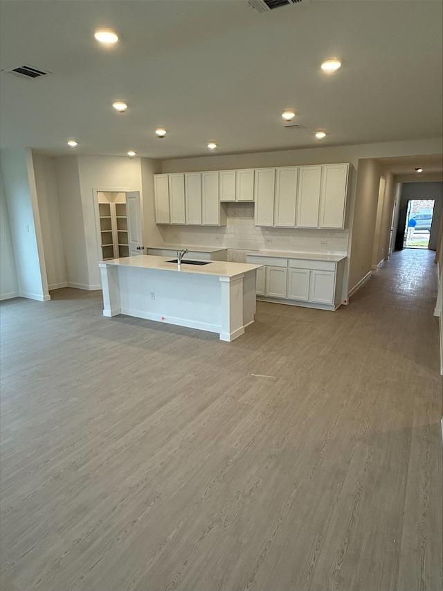 kitchen with sink, white cabinetry, tasteful backsplash, a center island with sink, and light wood-type flooring