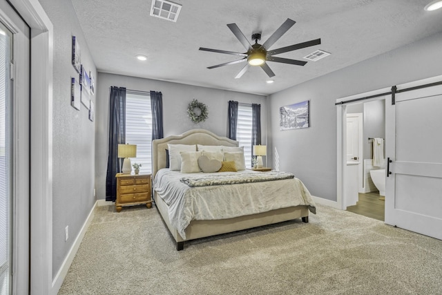 bedroom with ensuite bath, a barn door, a textured ceiling, and carpet flooring