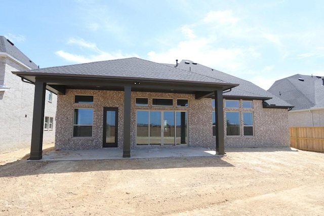 back of house with brick siding, fence, roof with shingles, and a patio area