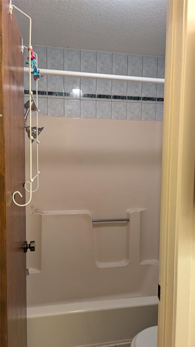 bathroom with bathtub / shower combination, toilet, and a textured ceiling