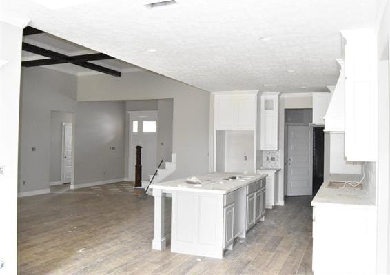 kitchen featuring hardwood / wood-style flooring, beam ceiling, an island with sink, white cabinets, and a kitchen bar