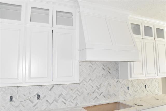 details with white cabinetry, premium range hood, backsplash, and light stone counters