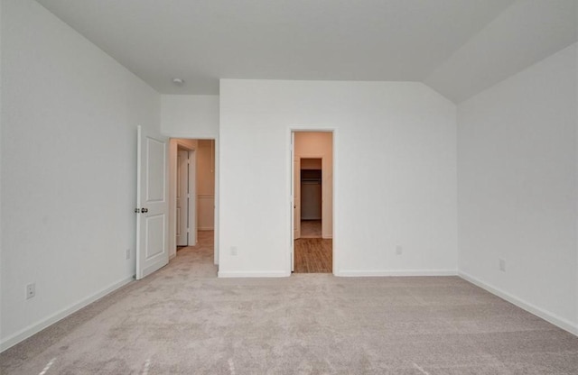 unfurnished bedroom featuring lofted ceiling, a walk in closet, and light colored carpet