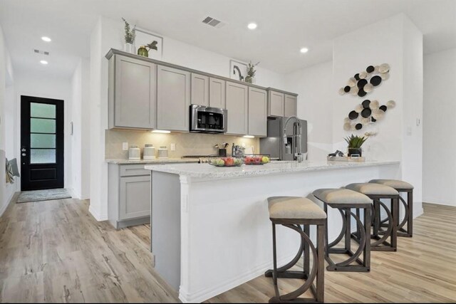 kitchen with stainless steel appliances, light stone countertops, gray cabinets, and light wood-type flooring