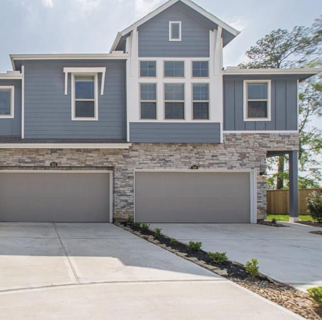 view of property with a garage, concrete driveway, stone siding, fence, and board and batten siding