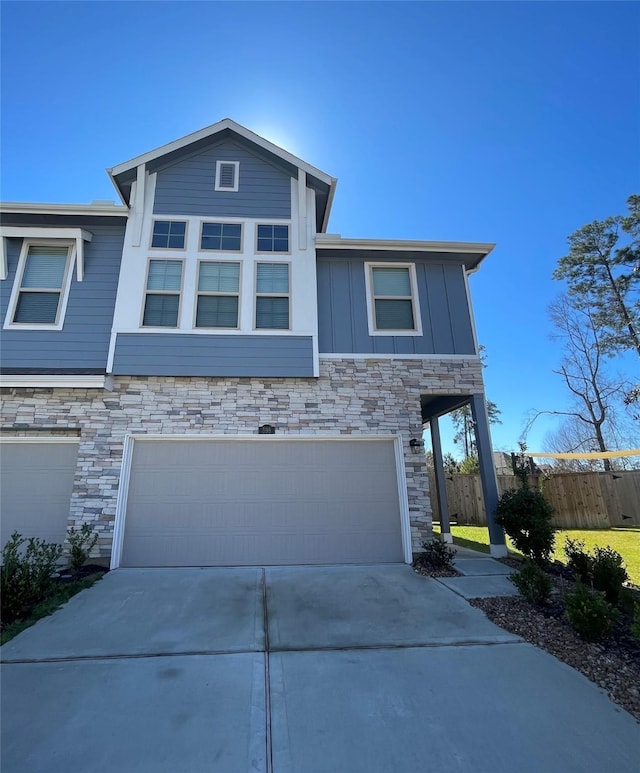 townhome / multi-family property featuring an attached garage, fence, concrete driveway, stone siding, and board and batten siding