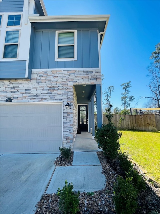 view of front facade featuring a garage, stone siding, fence, board and batten siding, and a front yard