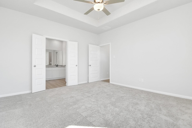 unfurnished bedroom featuring connected bathroom, sink, light colored carpet, ceiling fan, and a raised ceiling