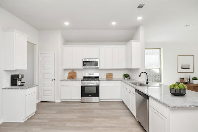 kitchen with appliances with stainless steel finishes, sink, white cabinets, and light stone counters