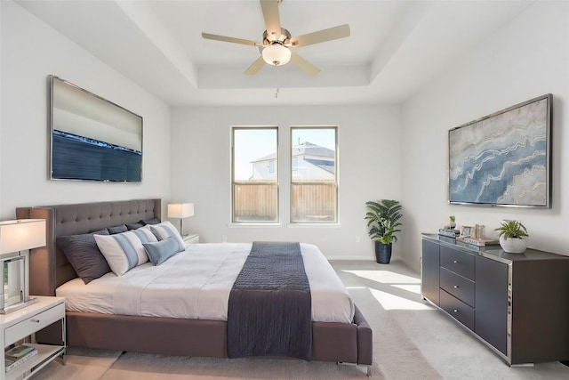 bedroom featuring ceiling fan, light colored carpet, and a raised ceiling