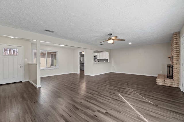 unfurnished living room featuring dark hardwood / wood-style flooring, a brick fireplace, a textured ceiling, and ceiling fan