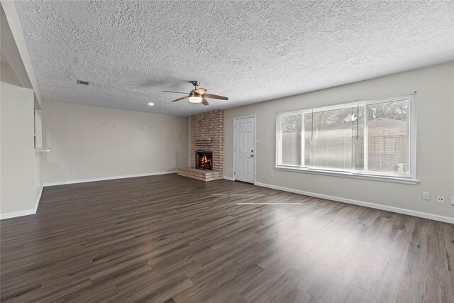 unfurnished living room featuring ceiling fan, dark hardwood / wood-style flooring, a brick fireplace, and a textured ceiling