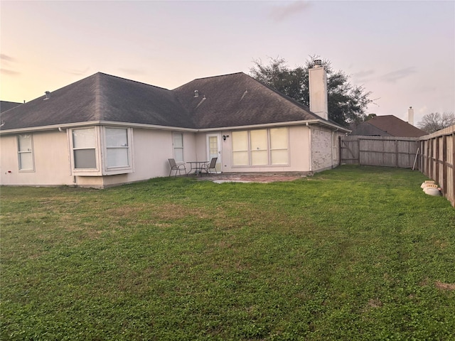 back house at dusk featuring a yard and a patio area