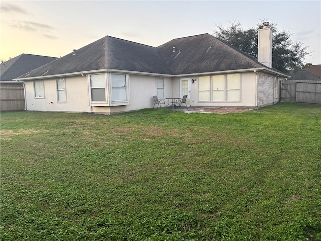 back house at dusk featuring a patio area and a lawn