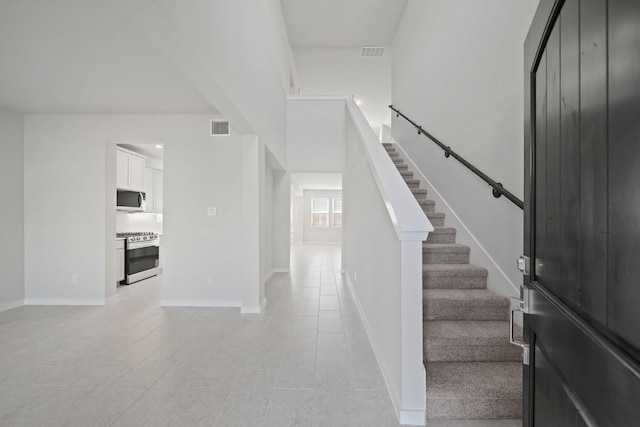 entrance foyer with stairs, baseboards, visible vents, and a towering ceiling