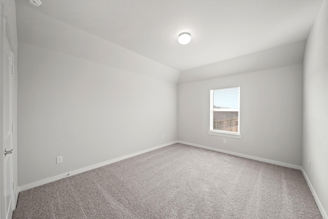 carpeted spare room featuring lofted ceiling and baseboards