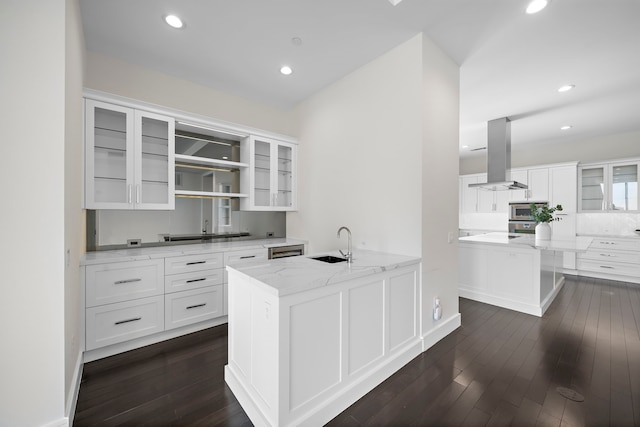 kitchen with sink, stainless steel microwave, light stone countertops, white cabinets, and island exhaust hood