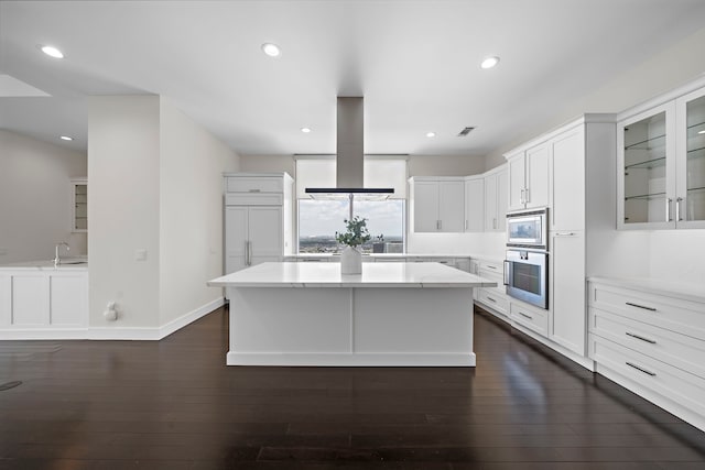 kitchen with white cabinetry, stainless steel appliances, island exhaust hood, a kitchen island, and dark hardwood / wood-style flooring