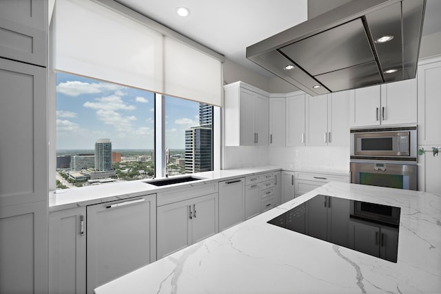 kitchen with wall chimney exhaust hood, sink, stainless steel appliances, light stone countertops, and white cabinets