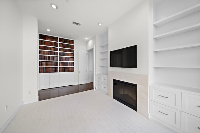 unfurnished living room featuring built in shelves and light colored carpet