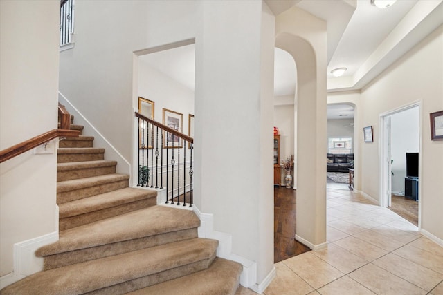 stairway with arched walkways, a towering ceiling, baseboards, and tile patterned floors