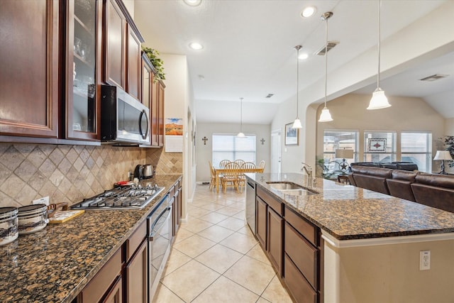 kitchen with sink, hanging light fixtures, dark stone counters, an island with sink, and stainless steel appliances