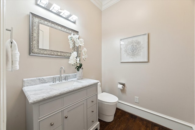 bathroom with vanity, wood finished floors, baseboards, crown molding, and toilet