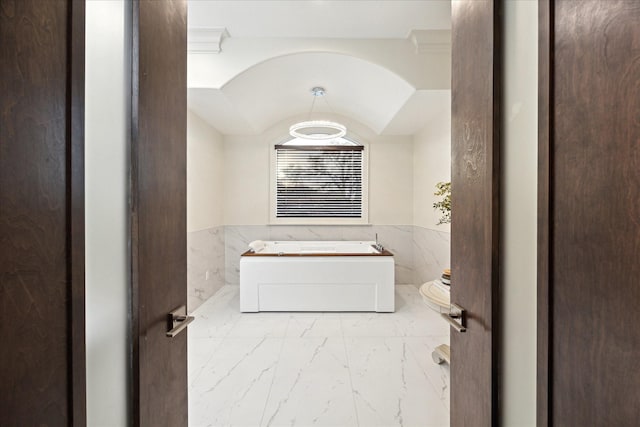 bathroom with a wainscoted wall, a garden tub, and marble finish floor