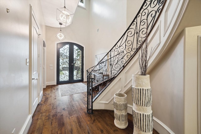 entryway featuring arched walkways, dark wood-style flooring, stairs, french doors, and a towering ceiling