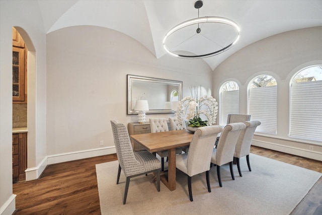 dining area with arched walkways, wood finished floors, baseboards, and vaulted ceiling