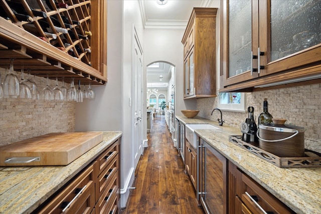 kitchen with beverage cooler, light stone countertops, arched walkways, ornamental molding, and glass insert cabinets