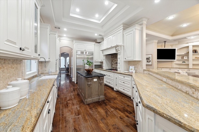 kitchen featuring a sink, a tray ceiling, light stone counters, arched walkways, and built in fridge