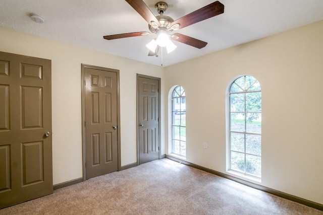 unfurnished bedroom featuring two closets, light colored carpet, and ceiling fan