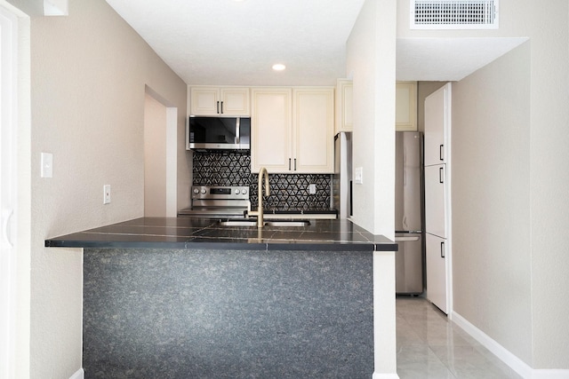 kitchen featuring sink, decorative backsplash, kitchen peninsula, stainless steel appliances, and cream cabinets