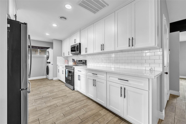 kitchen featuring stacked washer and dryer, light stone counters, appliances with stainless steel finishes, white cabinets, and backsplash