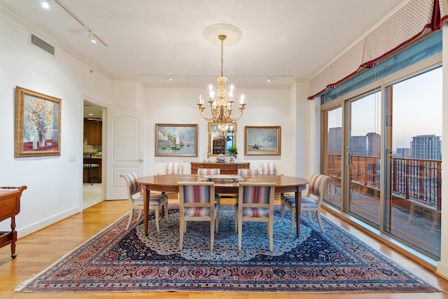 dining area with crown molding, track lighting, an inviting chandelier, and light wood-type flooring