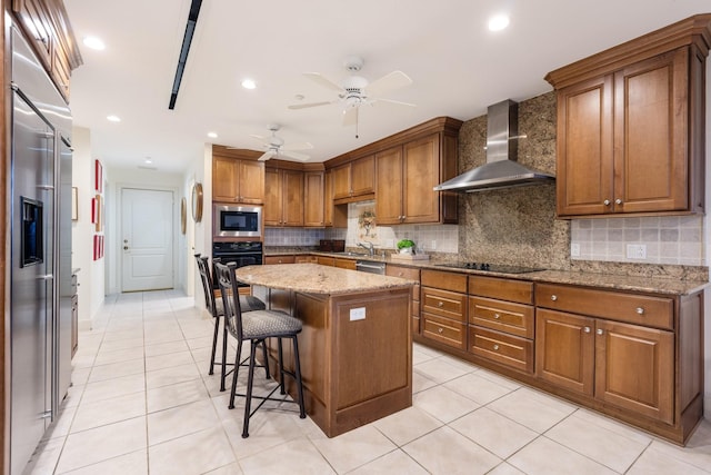 kitchen with a kitchen island, a breakfast bar area, light stone counters, black appliances, and wall chimney exhaust hood