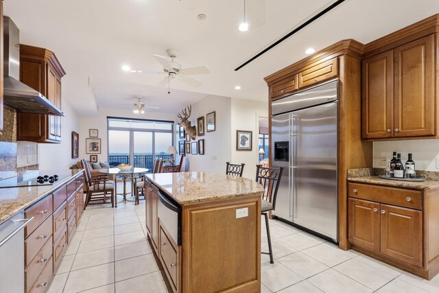 kitchen with a center island, black electric cooktop, a kitchen breakfast bar, built in fridge, and wall chimney range hood