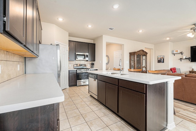 kitchen featuring sink, light tile patterned floors, appliances with stainless steel finishes, tasteful backsplash, and a center island with sink